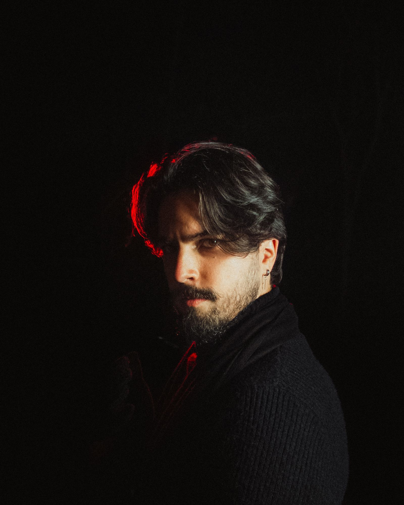 A bearded man lit by red accent light in a dark room.