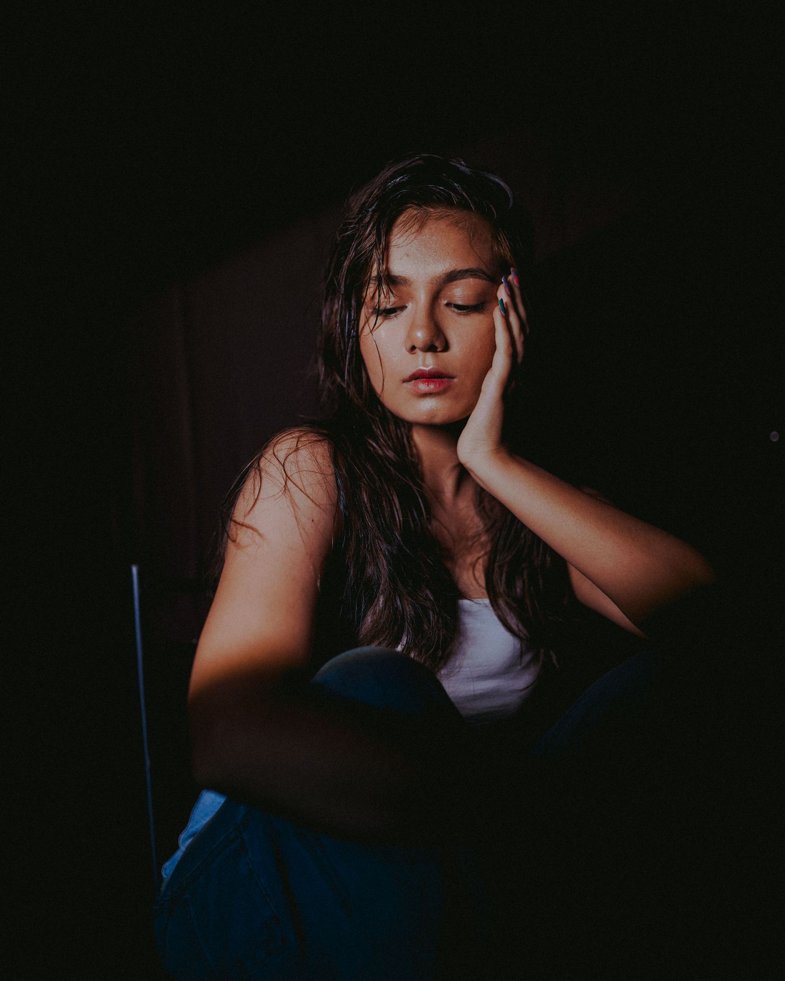 A woman sitting with eyes closed under a single studio spotlight.